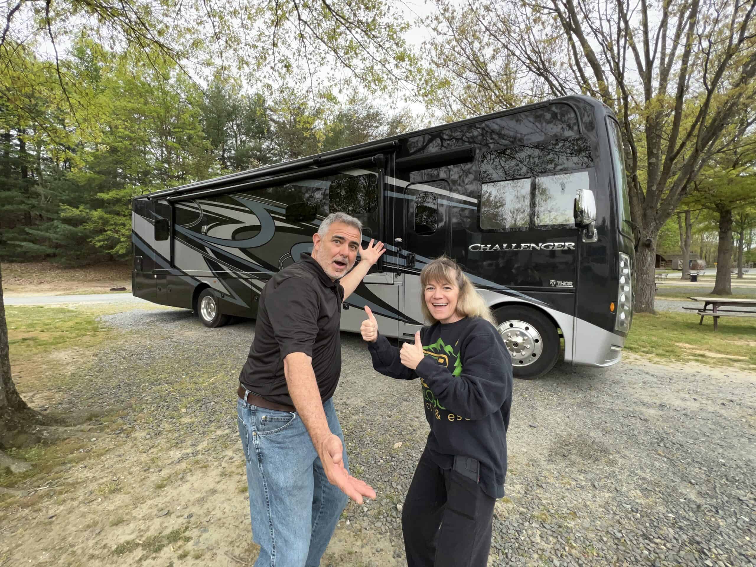 mike and susan from RVBlogger in front of and pointing towards their Class A RV